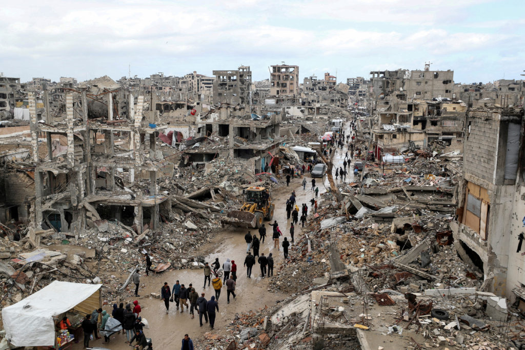 FILE PHOTO: Palestinians walk past the rubble of buildings destroyed during the Israeli offensive, on a rainy day, amid a ...