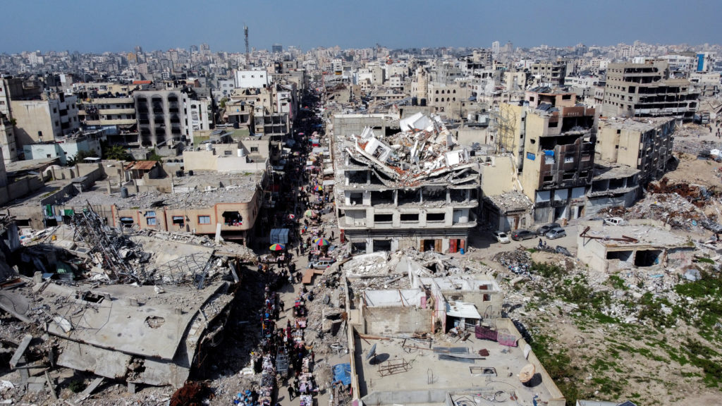 A drone view shows Palestinians walking at a street market near buildings damaged and destroyed during the Israeli offensi...