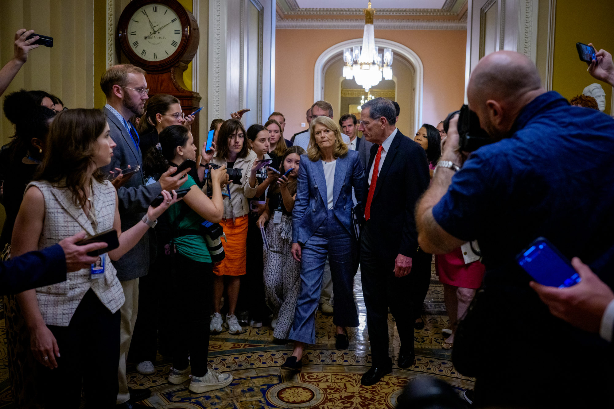 Sen. Lisa Murkowski, R-Ala., (center) and Sen. John Barrasso, R-Wy., (center right), walk toward the Senate floor, past journalists, to get President Donald Trump's big bill through Congress.