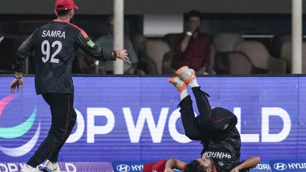 Afghan cricketers celebrating a win, one player is airborne, with a digital scoreboard in the background.