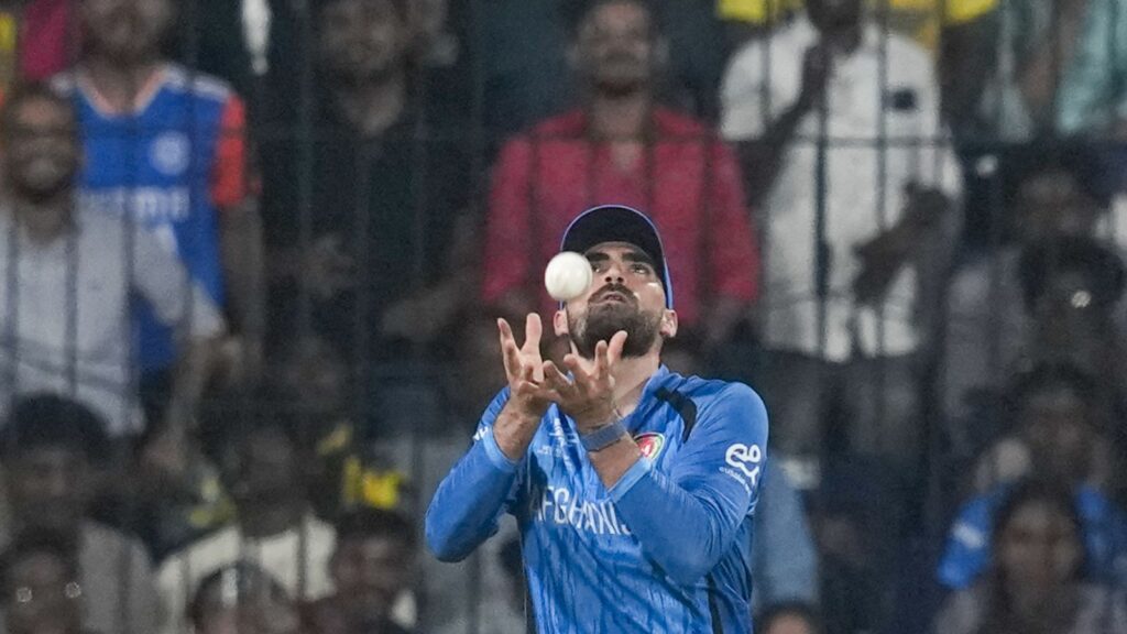 Afghan cricket player catches the ball during a match, with fans cheering in the background.