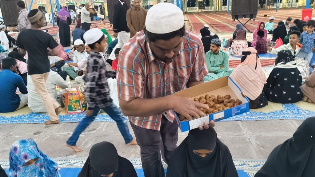 Man serving dates during Iftaari at Makkah Masjid with community members gathered.