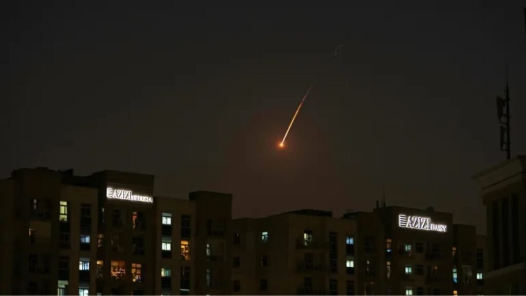 Meteor streaking across night sky above city buildings during missile attack.