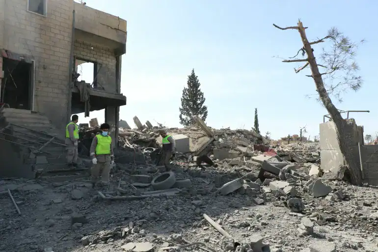 Rescue workers in safety vests examine destruction caused by recent conflict, debris scattered across the.