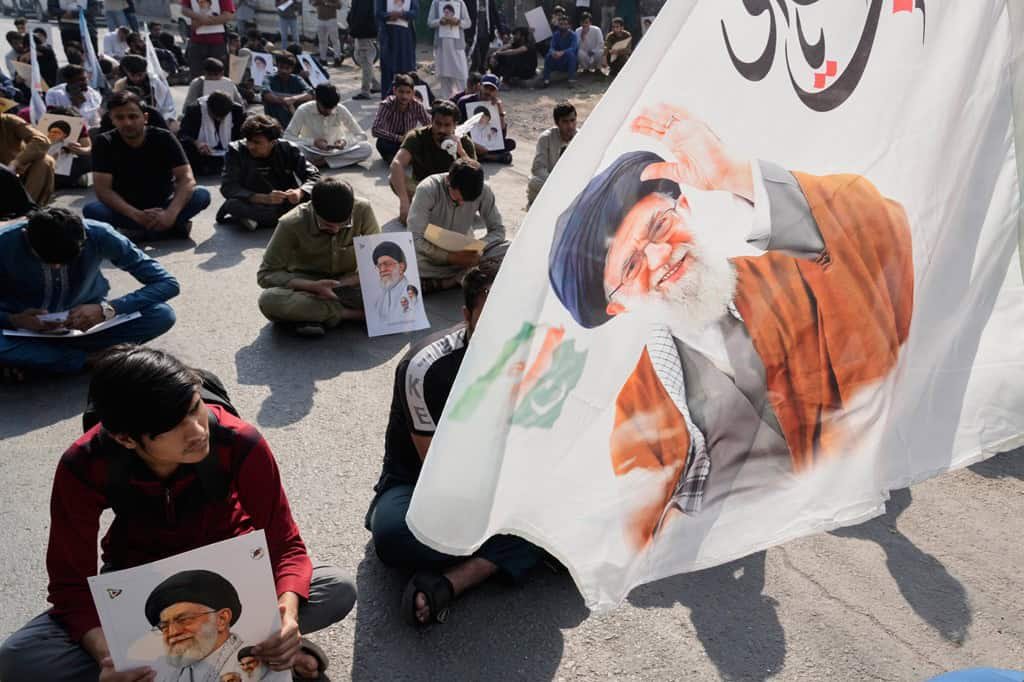 Shiite Muslims sit on a road holding portraits during a protest in Lahore.