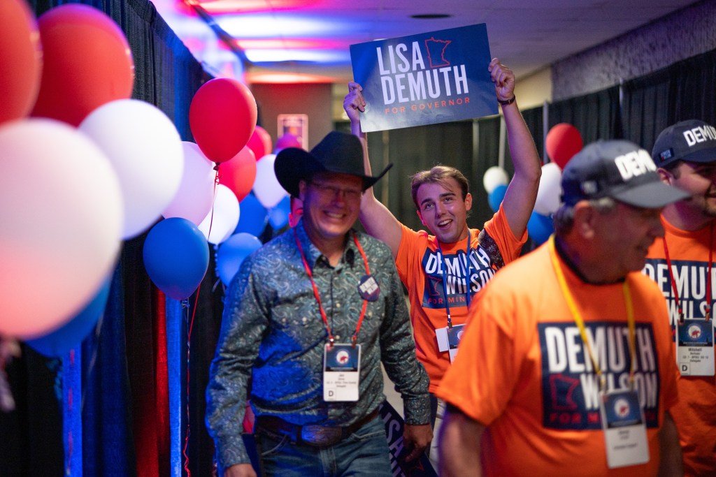 People walk through a hallway holding signs and wearing political t-shirts.