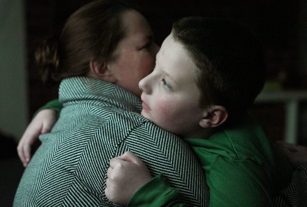 young boy wearing a green shirt hugging a woman wearing a patterned sweater